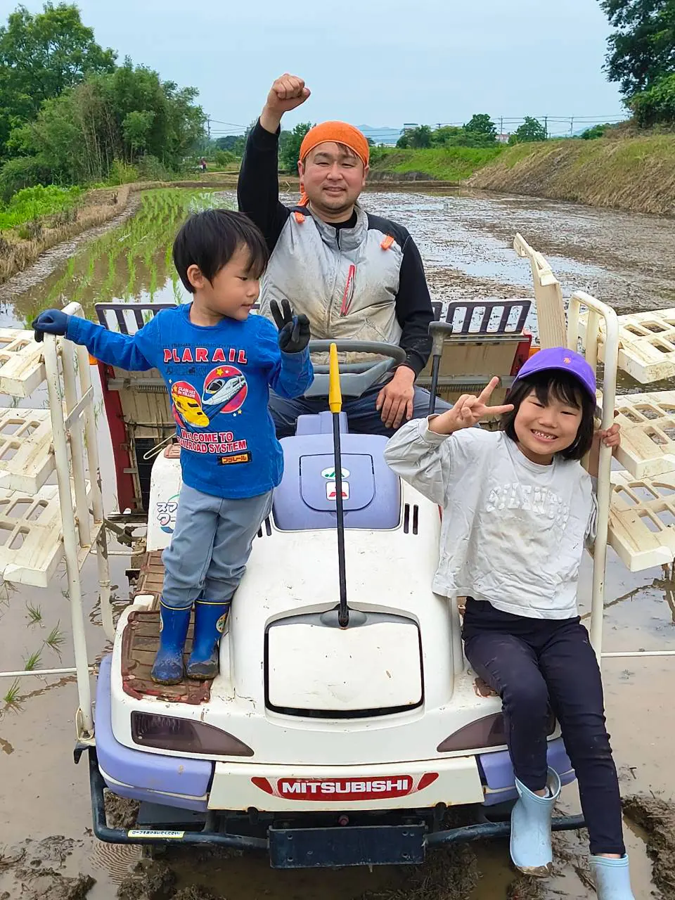 田植え機の上で、中島 紳児と子どもたちが田んぼにいる様子